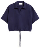 A cropped short-sleeve knit polo shirt in deep navy blue, featuring a collar, a split V-neckline, and a drawstring tie at the hem, displayed against a clean off-white background.