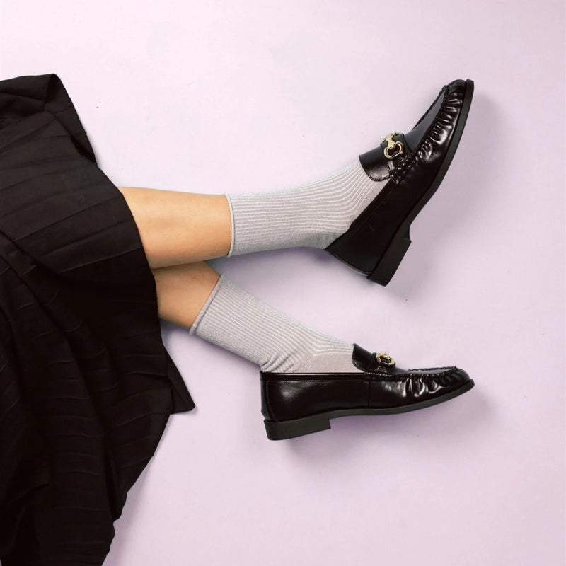 Black loafers worn with light grey glitter socks on a light pink background