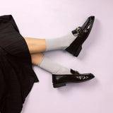 Black loafers worn with light grey glitter socks on a light pink background